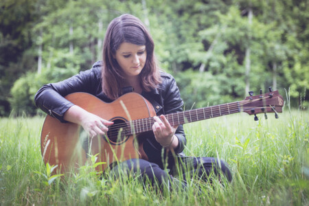 Photo : Élise Schipman Clem jouant de la guitare assise dans l'herbe