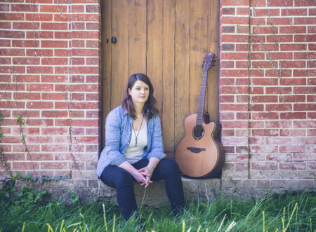 Photo : Élise Schipman Clem assise devant une porte et un mur de briques