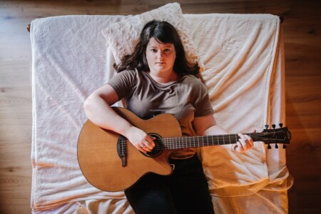 Photo : Élise Schipman Clem jouant de la guitare allongée sur un lit
